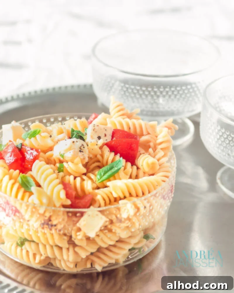 A vibrant Caprese pasta salad featuring pasta, cherry tomatoes, fresh mozzarella balls, basil leaves, and capers, glistening with dressing.