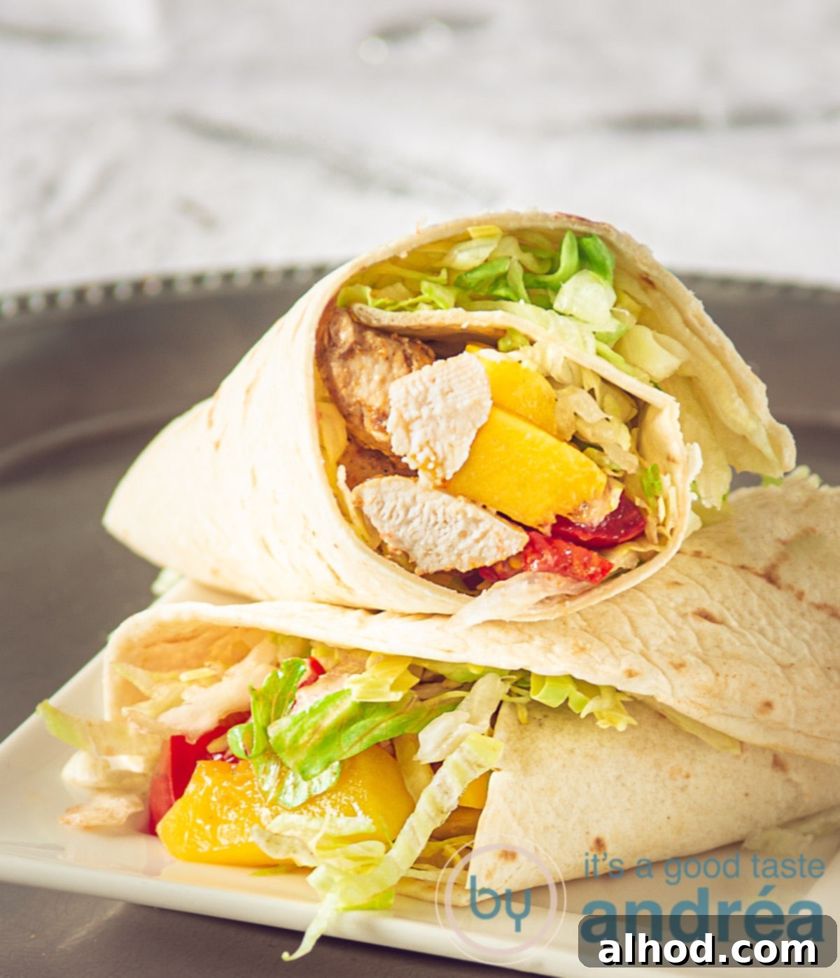 Two vibrant wraps generously filled with tender spicy chicken, sweet mango, crisp lettuce, and fresh tomato, presented on a sleek silver plate.