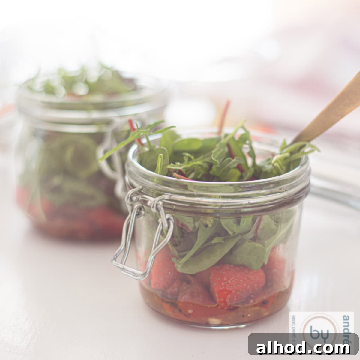 Two charming jars filled with layers of fresh summer salad ingredients, including crisp lettuce, bright strawberries, and a honey mustard dressing at the bottom.