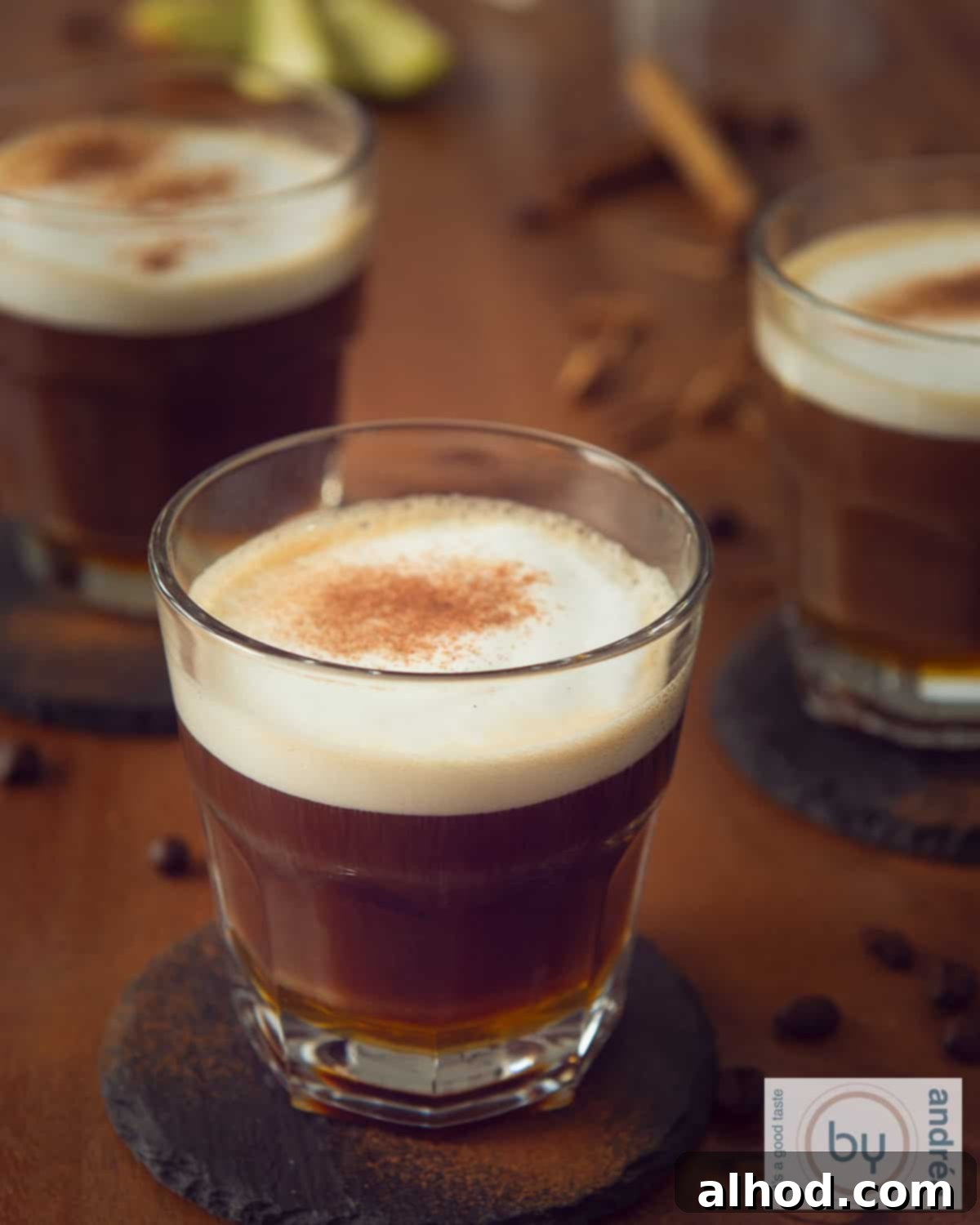 Spiced Honey Apfelkorn Latte 2 A brown table with three cups of creamy Apfelkorn latte with honey and cinnamon.