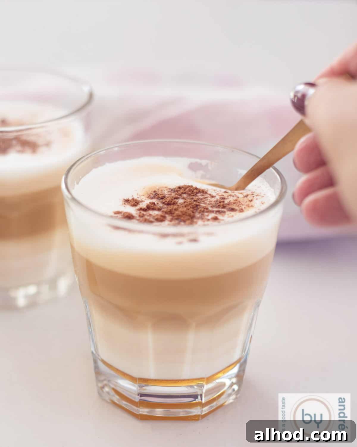 Spiced Honey Apfelkorn Latte 3 Two clear glasses of Apfelkorn latte with honey and milk on a white background, garnished with cinnamon.