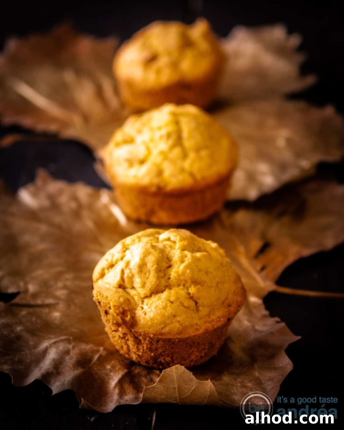 Golden Fluffy Cornbread Muffins Made Simple 3 Three golden brown cornbread muffins arranged artfully on a bed of vibrant autumn leaves, hinting at their perfect place on a festive holiday table.