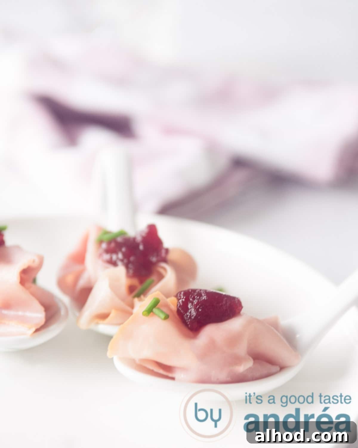 Sweet & Savory Ham Cranberry Morsels 5 Two small, elegant plates, each presenting a perfectly portioned ham and cranberry amuse-bouche, are artfully placed on a rich red carpet, enhancing the festive atmosphere.