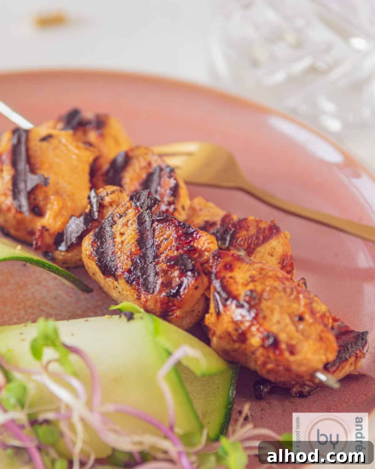 An aerial photo of two chicken skewers marinated in ketjap and mustard on a pink plate. A cucumber salad is served with it.
