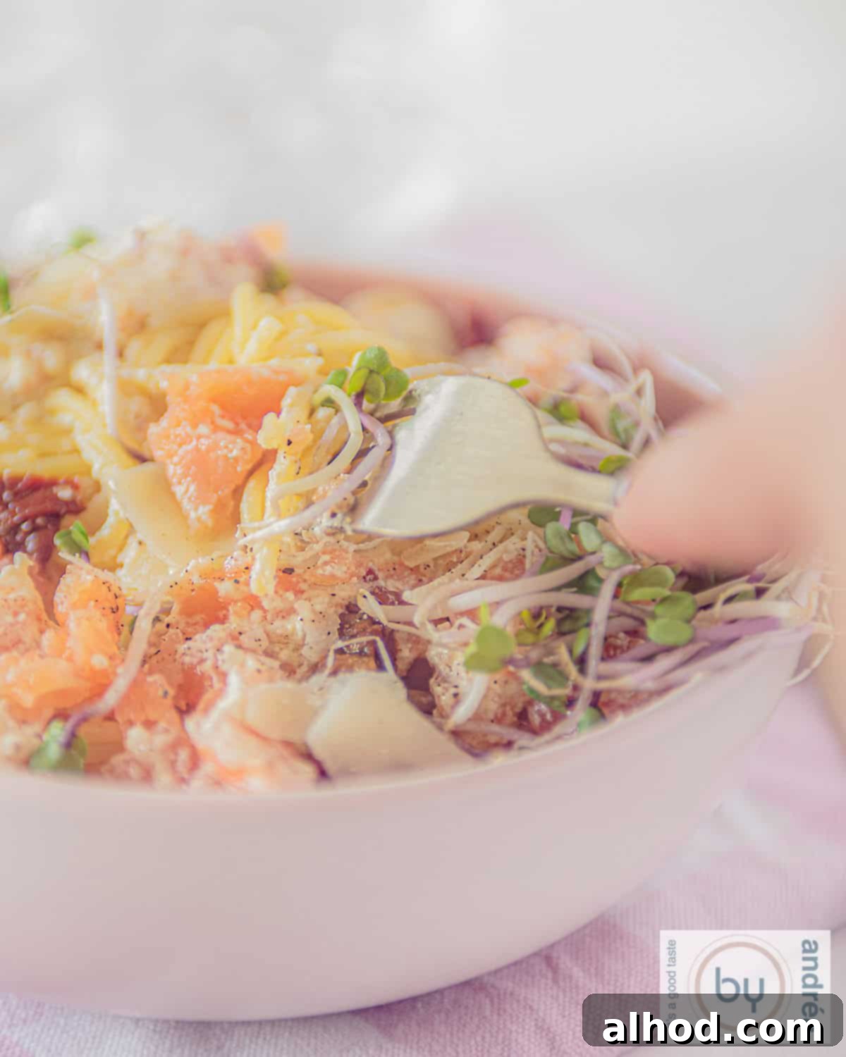 Velvety Smoked Salmon Pasta 2 A vibrant pink bowl brimming with al dente spaghetti, generous flakes of smoked salmon, slices of sun-dried tomatoes, and a dollop of creamy crème fraîche. A fork gently lifts a portion of the pasta, inviting a delightful bite.