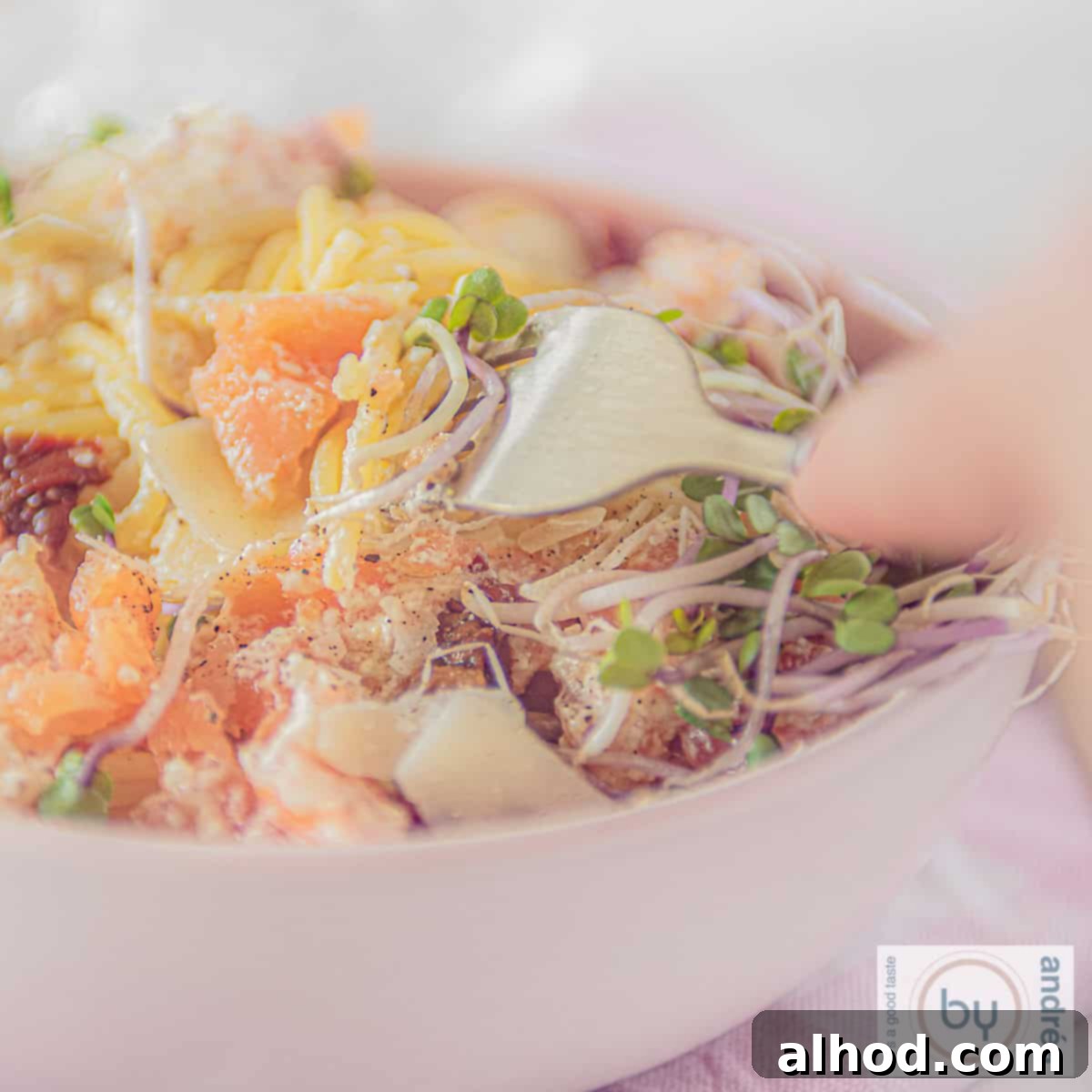 Velvety Smoked Salmon Pasta 4 A square photo of a creamy pasta dish featuring spaghetti, smoked salmon, and a sprinkle of Parmesan cheese, ready to be enjoyed. A fork gently lifts a strand.