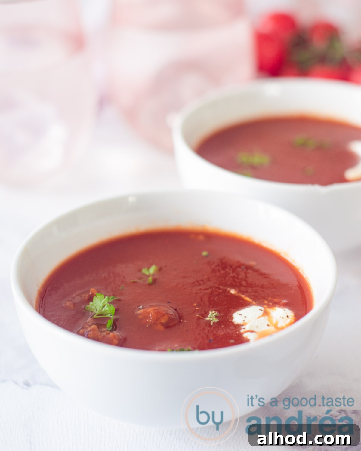 Two bowls of tomato soup with meatballs, cream, and fresh parsley. Two spoons in the background.
