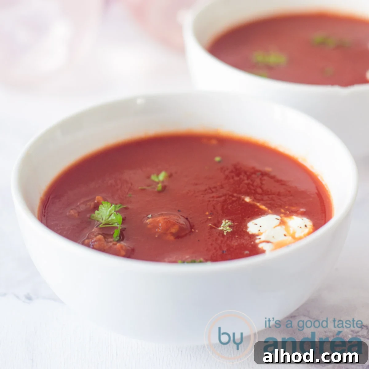 Authentic Dutch Tomato Meatball Soup 4 A square photo of two bowls of tomato, cream and parsley soup