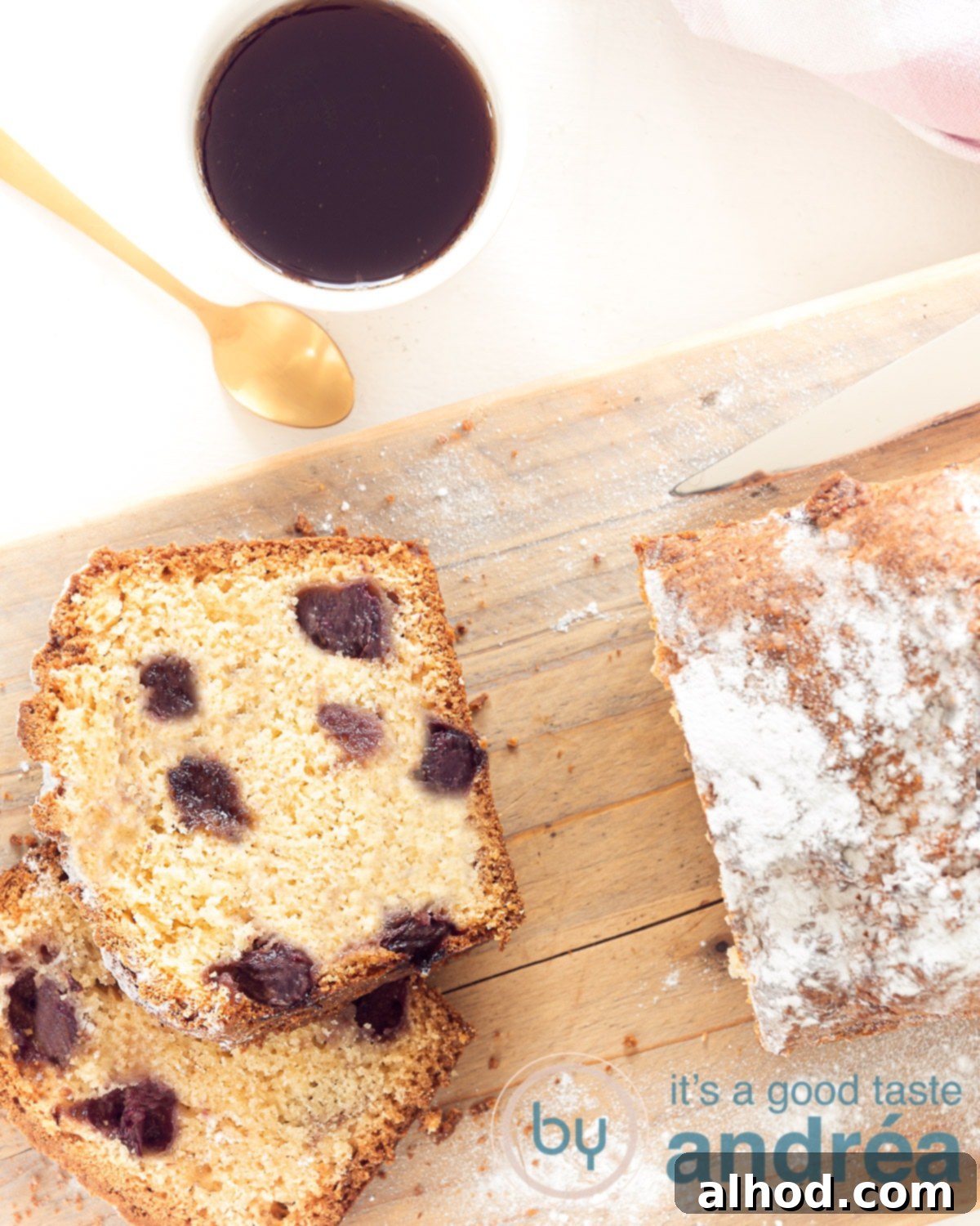 Tangy Blueberry Yogurt Cake 2 A beautifully baked blueberry yogurt cake on a wooden board, with two slices already cut, next to a cup of coffee with a golden spoon. The cake is rich with blueberries and appears incredibly moist and fluffy.