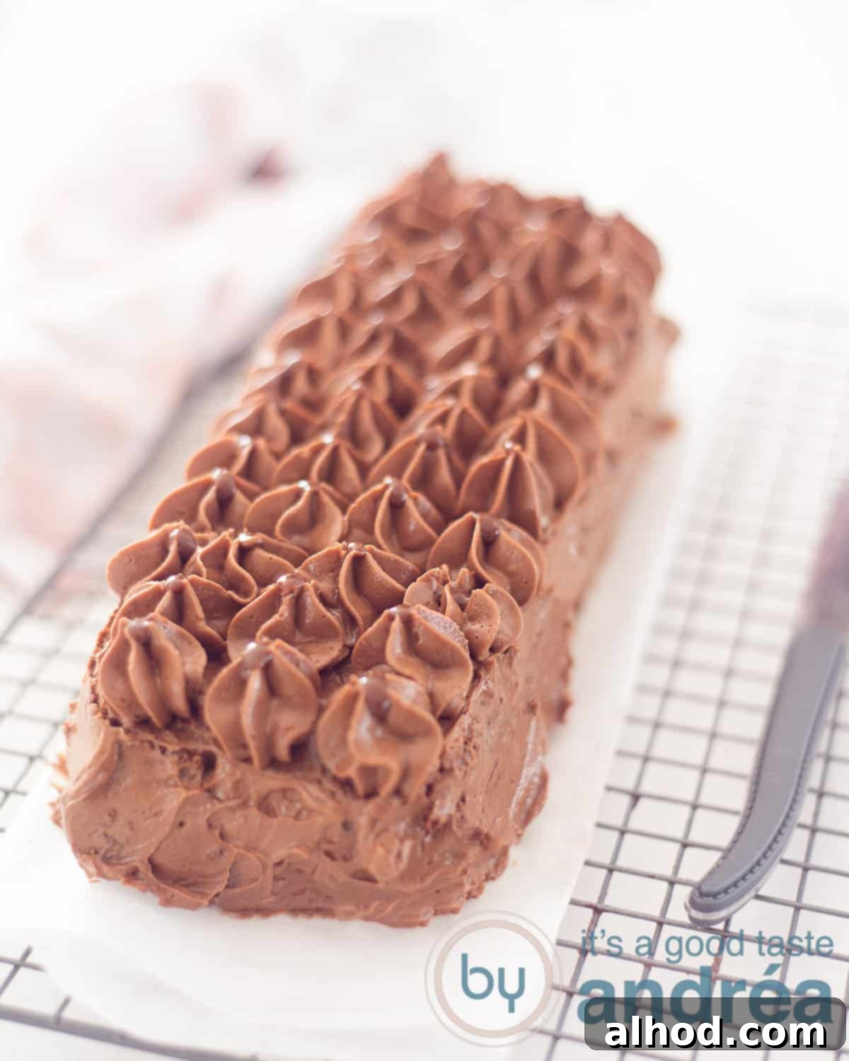 Decadent Chocolate Loaf 2 A chocolate cream truffle cake on a white baking paper on a baking rack. a knife is right next to it.