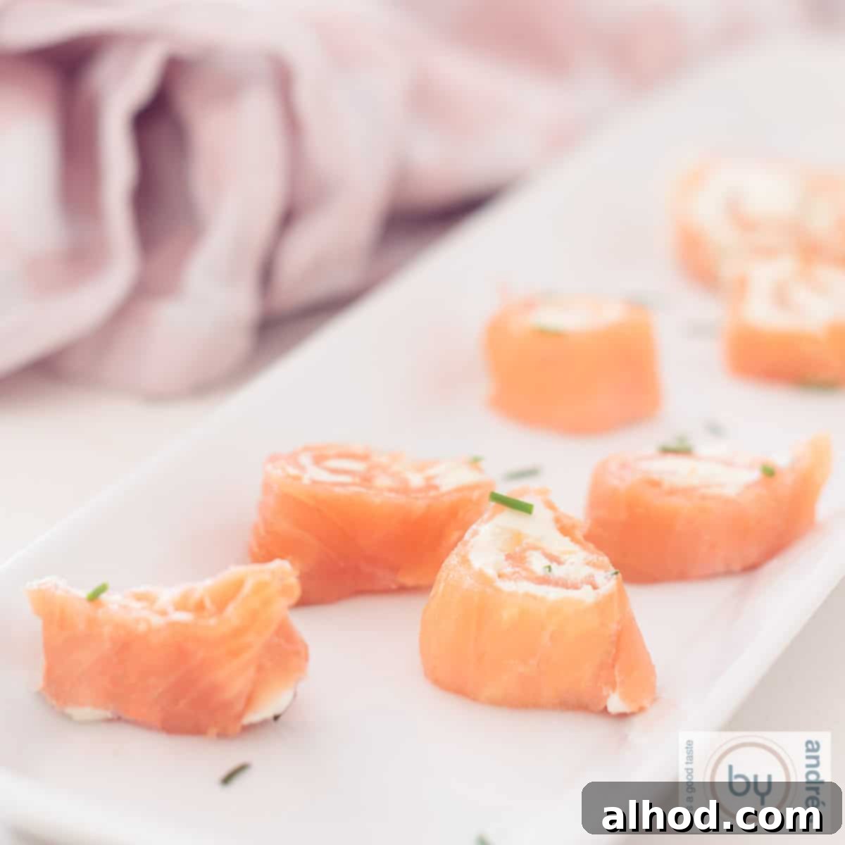 A square photo showing part of a long tray of salmon rolls filled with cream cheese and chives
