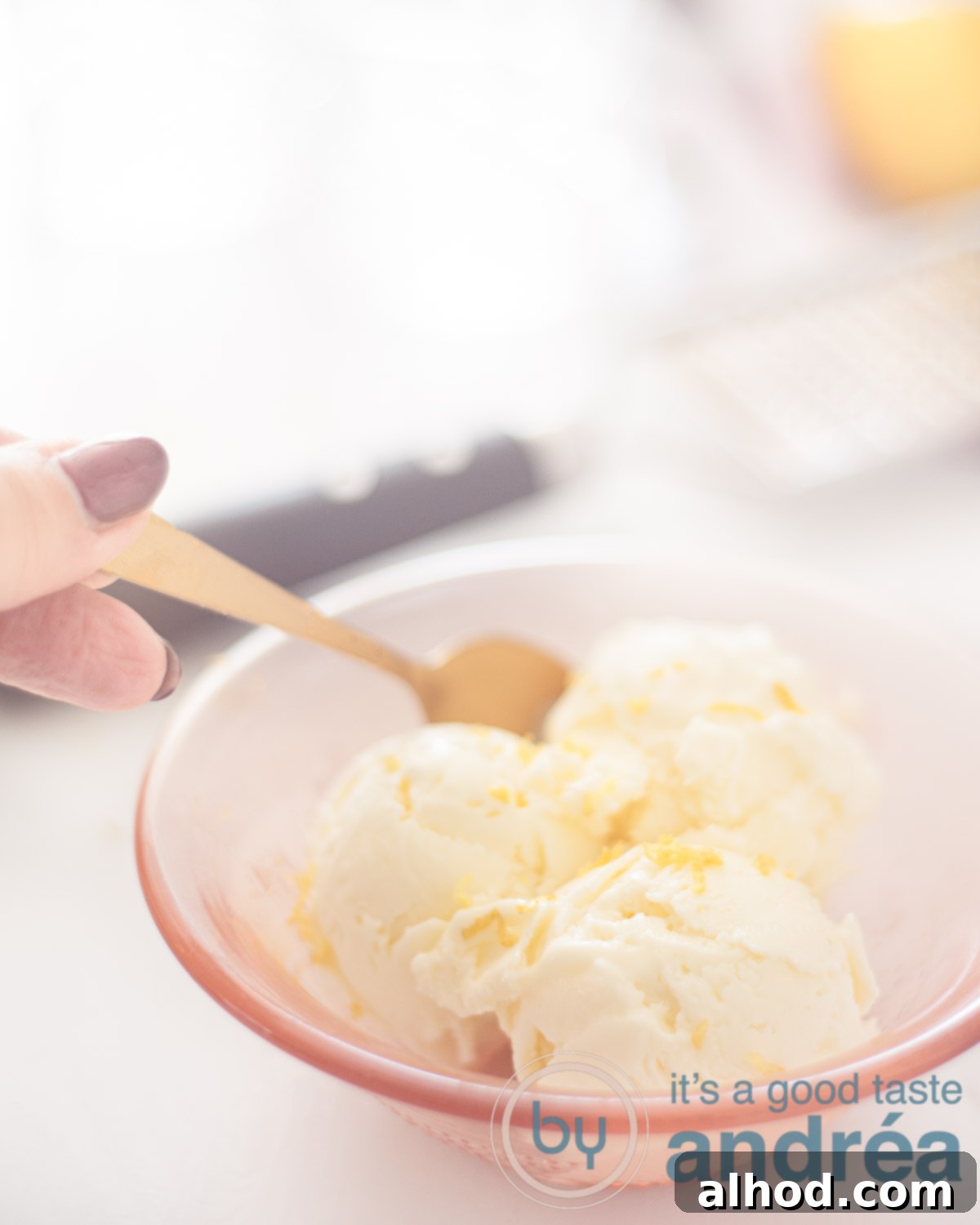 Three scoops of creamy lemon ice cream in an orange bowl, with a golden spoon digging into a scoop.
