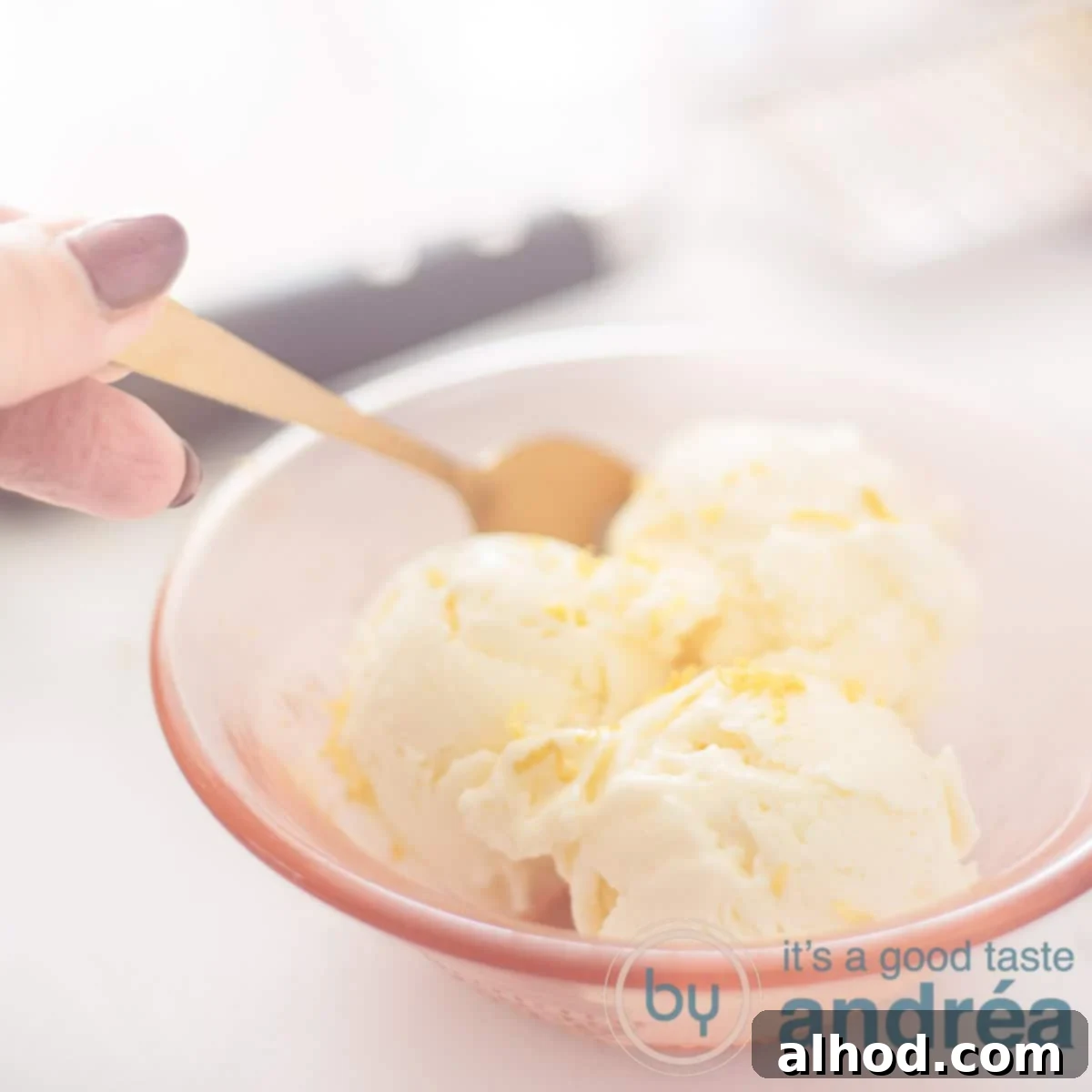 A square photo with homemade lemon ice cream in an orange bowl. A spoon takes a bite. A grater in the background