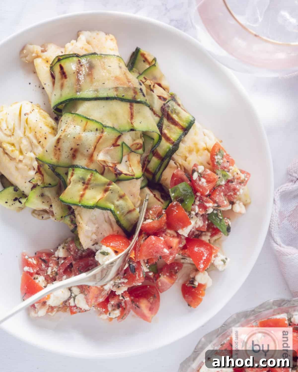 Golden Tilapia with Fresh Tomato Feta Salad 3 A photo from above with a white plate, 3 fried tilapias wrapped in zucchini at the top, a tomato feta salsa at the bottom.