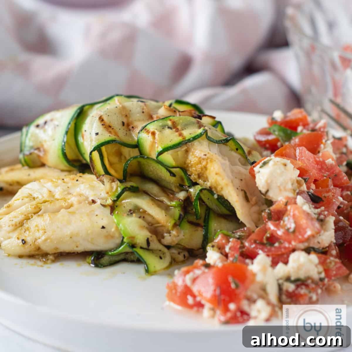Golden Tilapia with Fresh Tomato Feta Salad 4 A square photo with a white plate on which is a tilapia fillet rolled in zucchini with a delicious tomato salad.