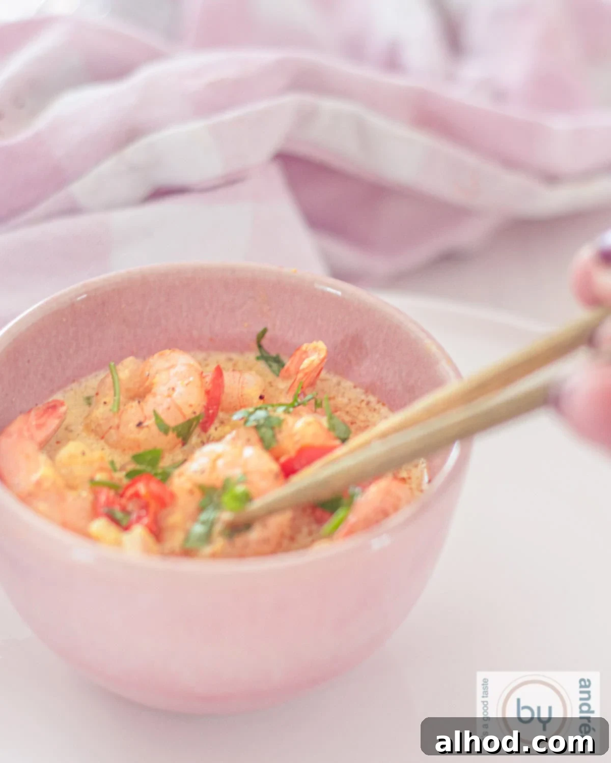 Simple Coconut Shrimp Curry with a Kick 3 A pink bowl with shrimp curry, red pepper and parsley. Two chopsticks pick out a shrimp.