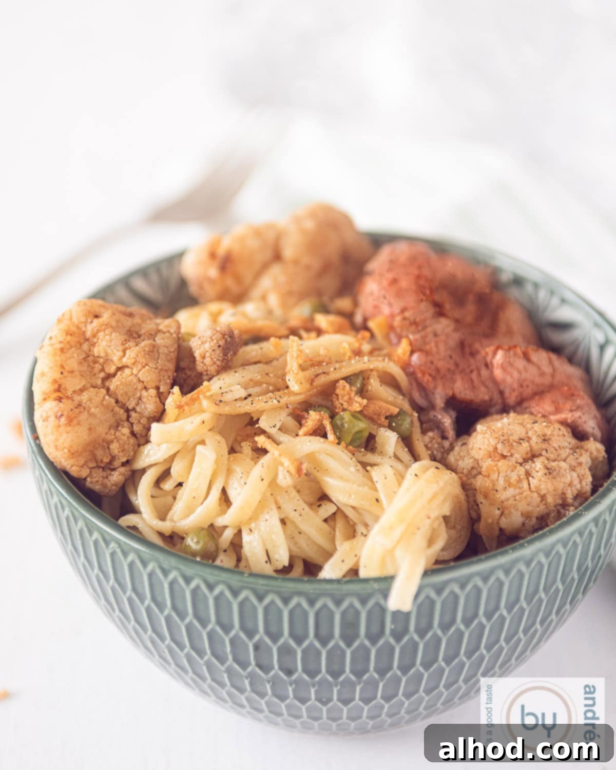 Hearty Beef and Cauliflower Noodle Bowl 3 A height photo with a green bowl with noodles in the front and steak in the back. Stir-fried cauliflower on both sides, garnished with fresh herbs.