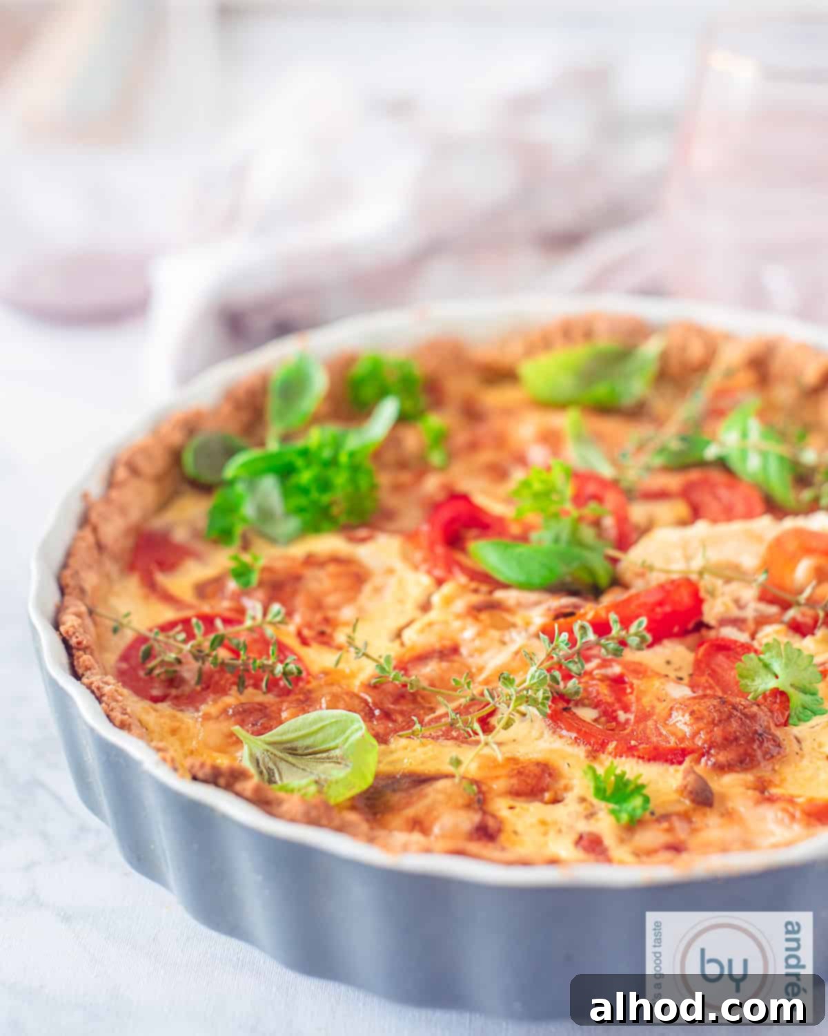 Savory Tomato Brie Quiche with Garden Herbs 2 Part of a grey quiche dish filled with a Brie, tomato and green herbs quiche