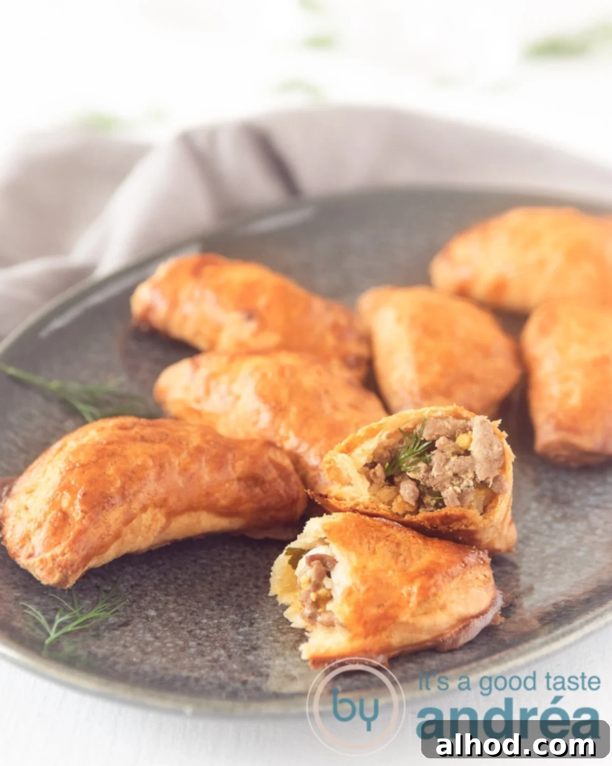 Classic Russian Piroshki 3 Russian priozhki on a grey plate. One appetizer is halved. Some dill is surrounding the platter