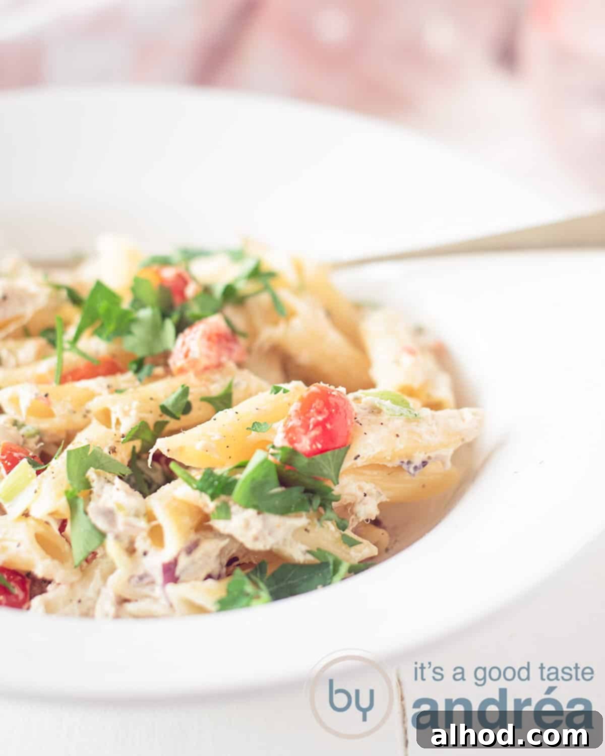 Velvety Smoked Mackerel Pasta 2 A height photo with half a white deep plate filled with pasta, smoked mackerel and vegetables in a herb cream cheese sauce. On a white background. In the background a pink and white tea towel.