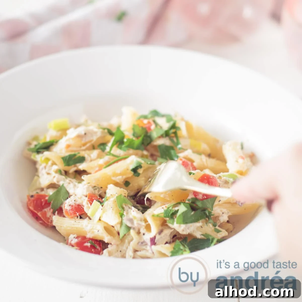 Velvety Smoked Mackerel Pasta 6 A square photo with a white deep plate filled with pasta, herb cream cheese and smoked mackerel and vegetables. A fork pricks the penne.