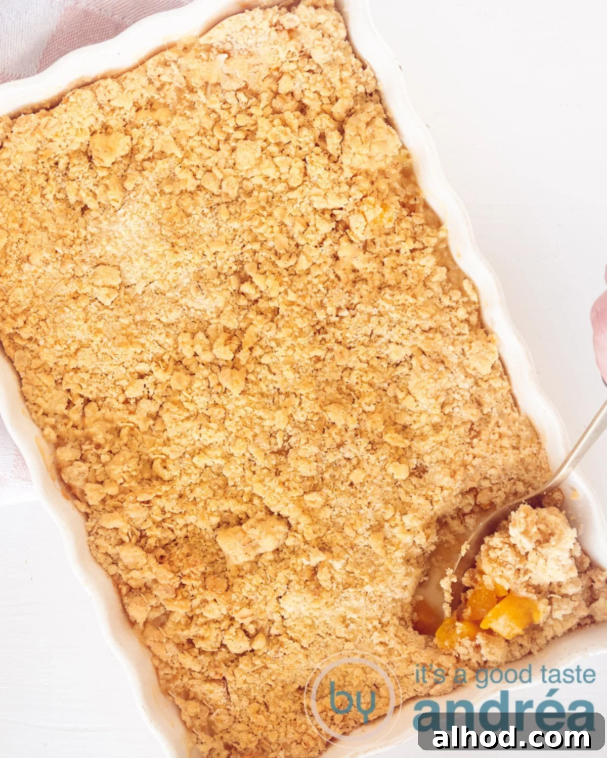 Golden Apple Peach Crumble 2 A warm, freshly baked Apple Peach Crumble in a white oven dish, with a spoon ready for serving. Overhead view.