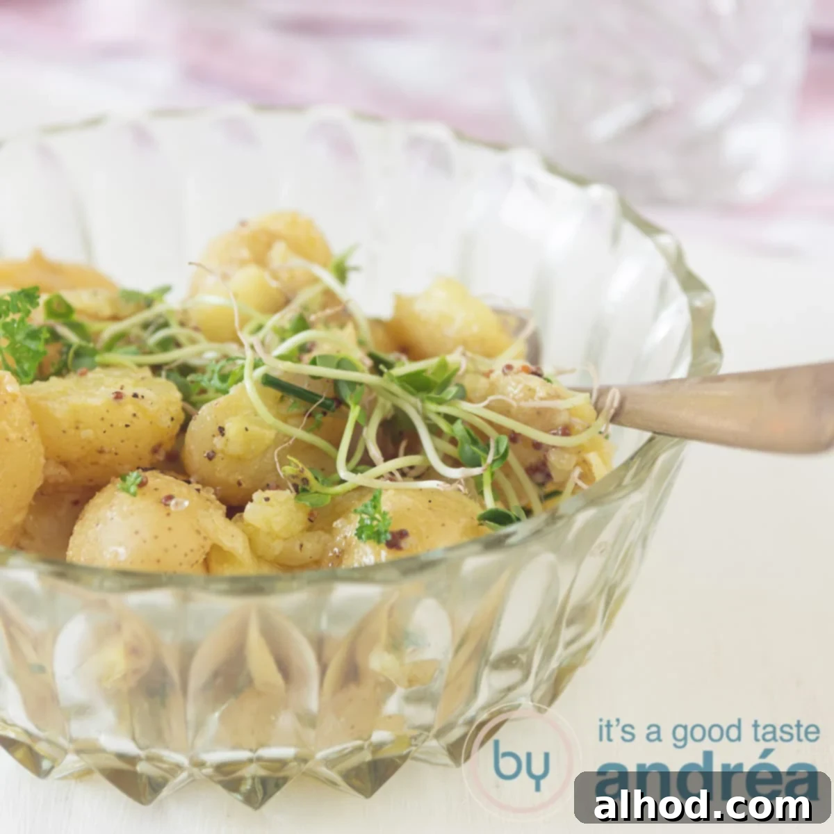 Velvety Baby Dutch Potato Salad 6 a square photo of a glass bowl filled with potato salad and some greens. A white backdrop and a pink white cloth in the back