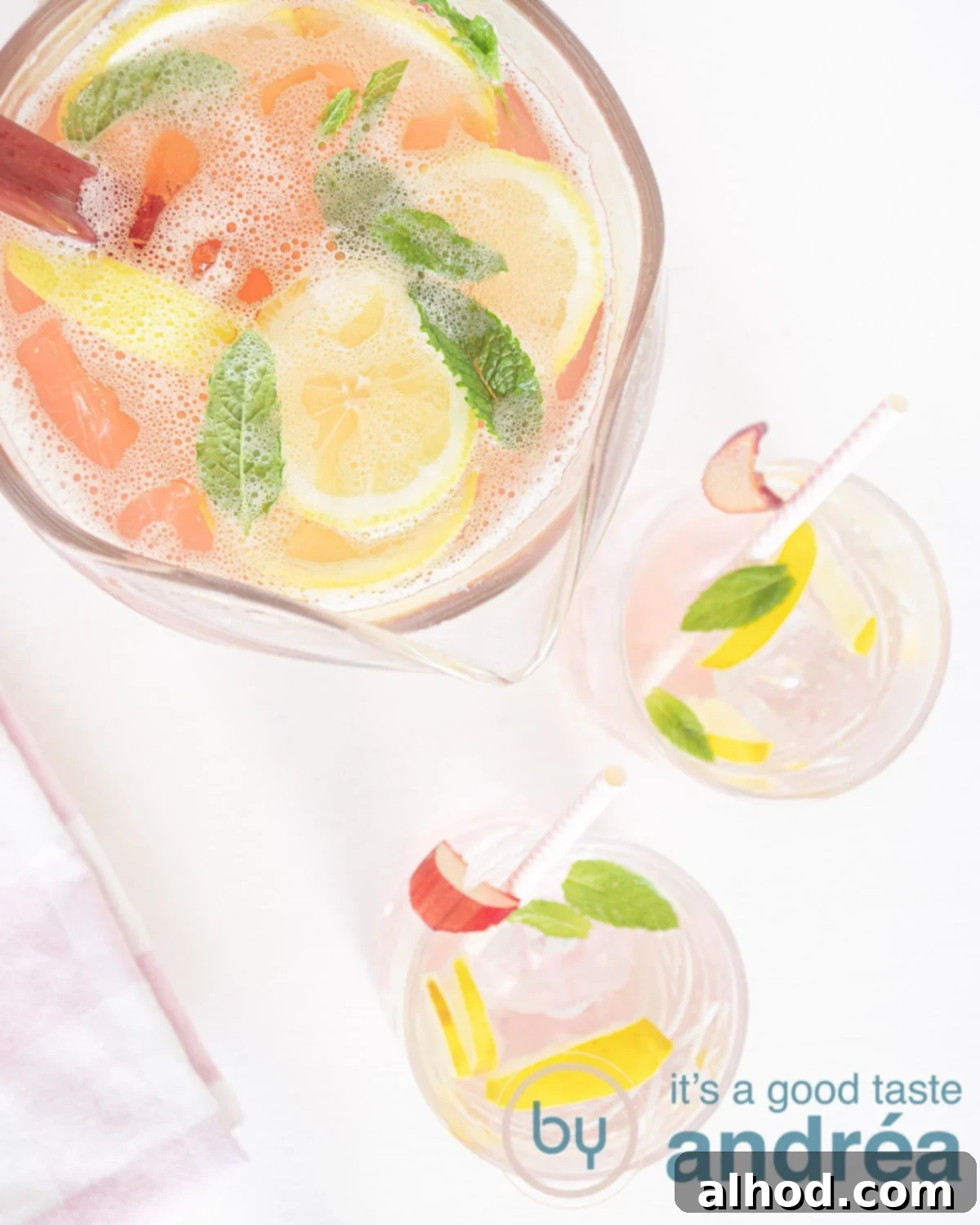 Tangy Rhubarb Refresher 2 A photo from above of a large jug of homemade Rhubarb Iced Tea with two glasses in front, garnished with lemon slices and mint, all placed on a crisp white background.