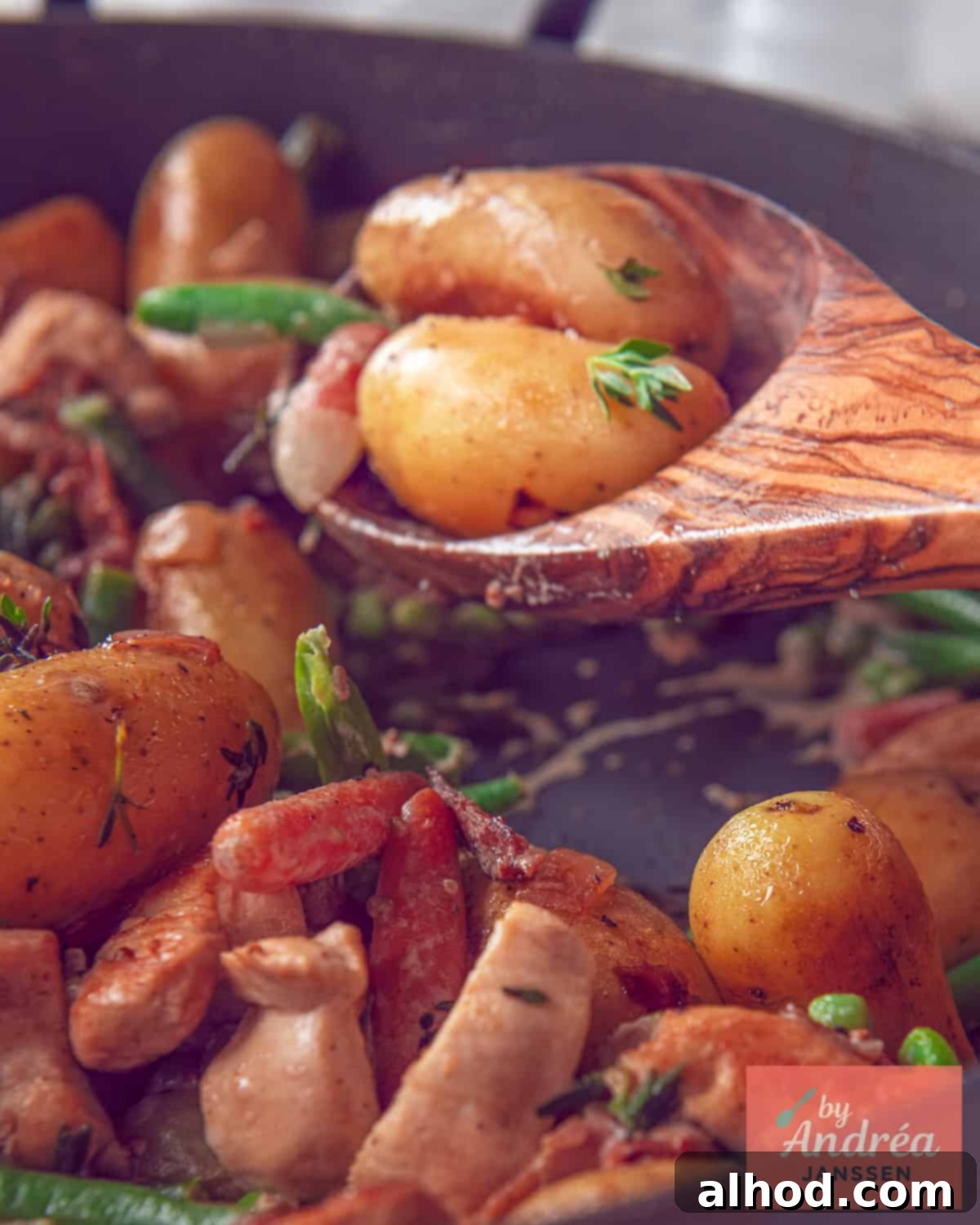 Golden Skillet Chicken with Crispy Bacon and Potatoes 2 A generous portion of a Chicken Potato Skillet, featuring golden-brown baby potatoes, tender chicken pieces, and colorful vegetables, all coated in a rich, creamy sauce. A wooden spoon is poised to scoop a serving, highlighting the texture and appeal of the dish.