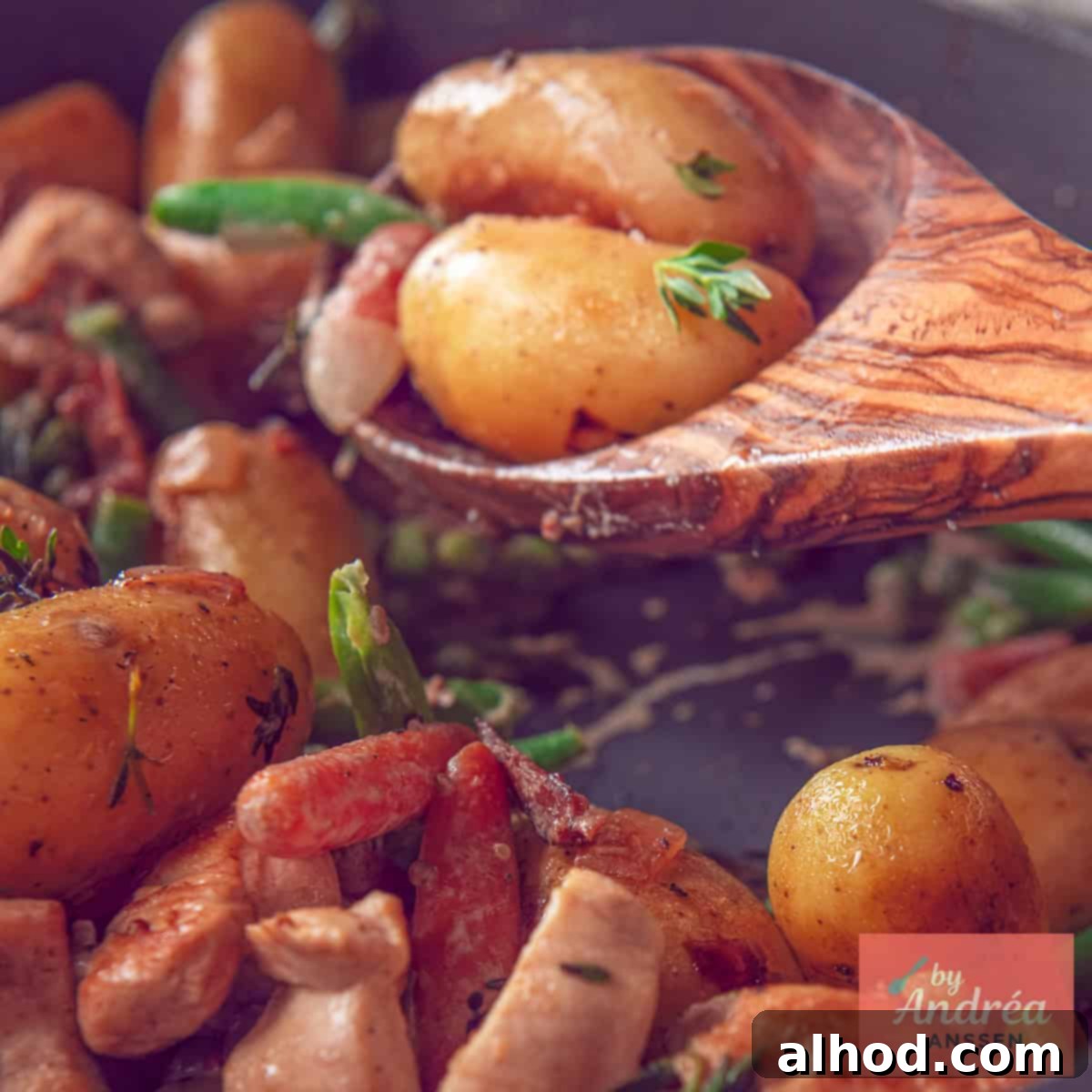 A square photo of a wooden spoon with potatoes, vegetables and chicken, showcasing the delicious result of the one-pan skillet meal.