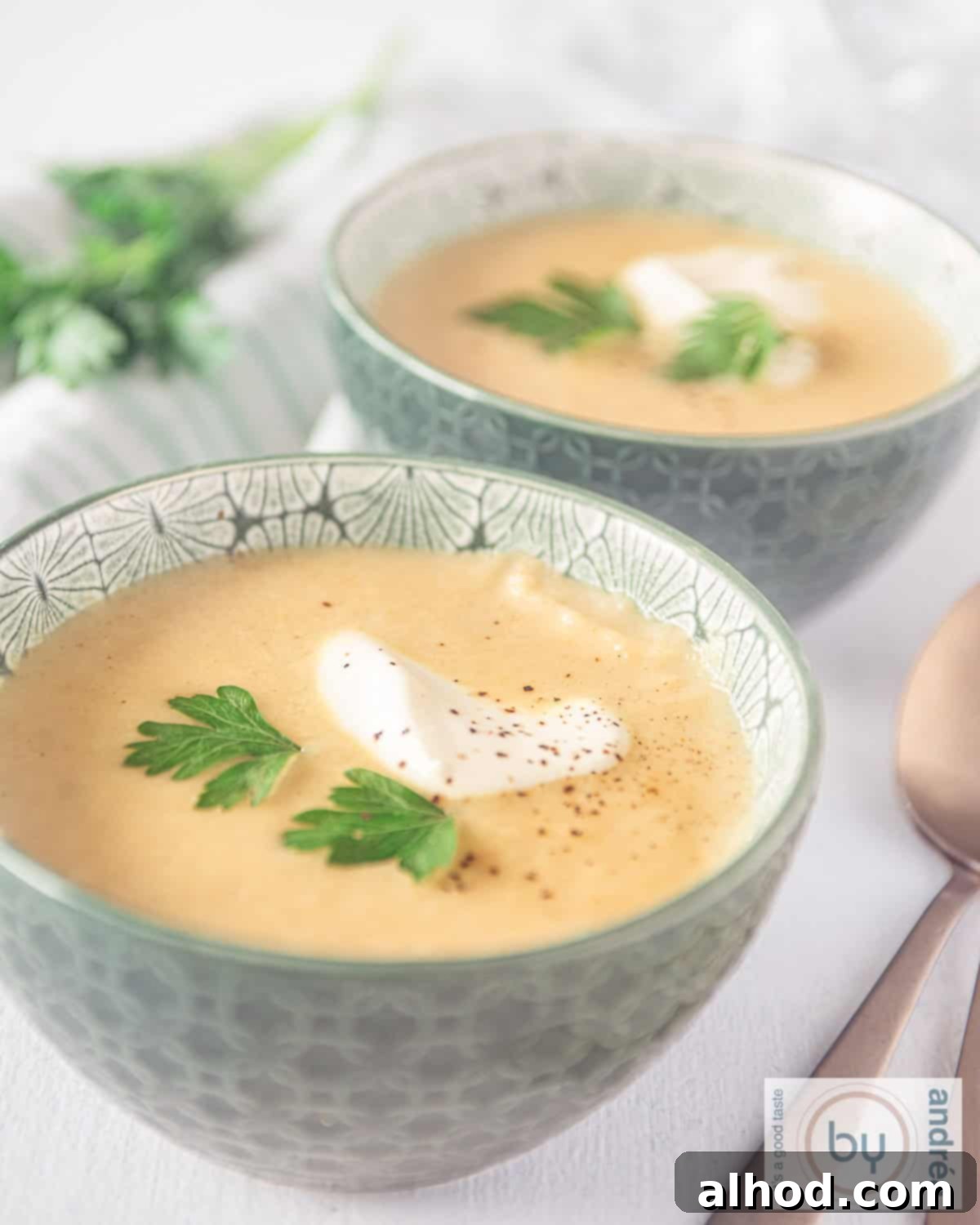 An aerial photo of two green bowls filled with parsnip soup, one behind the other. A garnish of yogurt and coriander.
