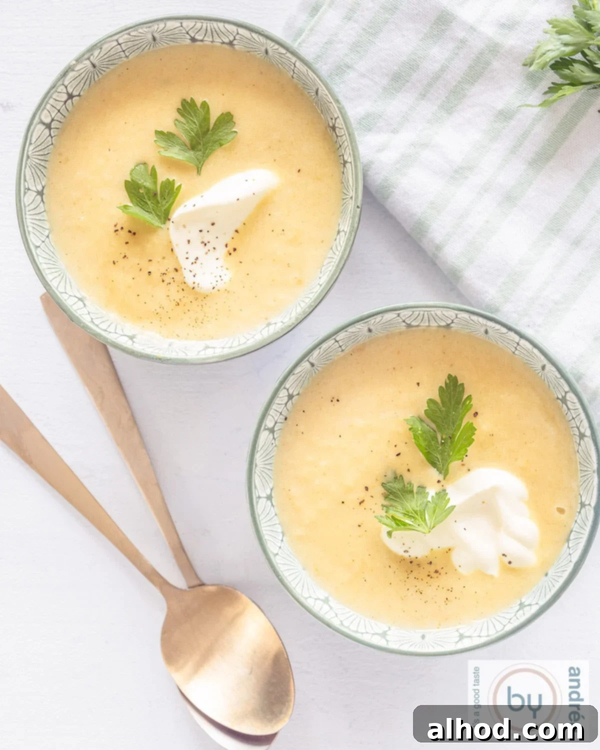A top-down photo of two bowls filled with parsnip soup with yogurt and cilantro. Two golden spoons lie beneath them.