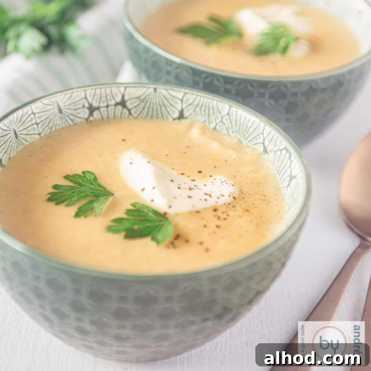 A square photo of two bowls of soup, filled with parsnip soup, cream and yoghurt.
