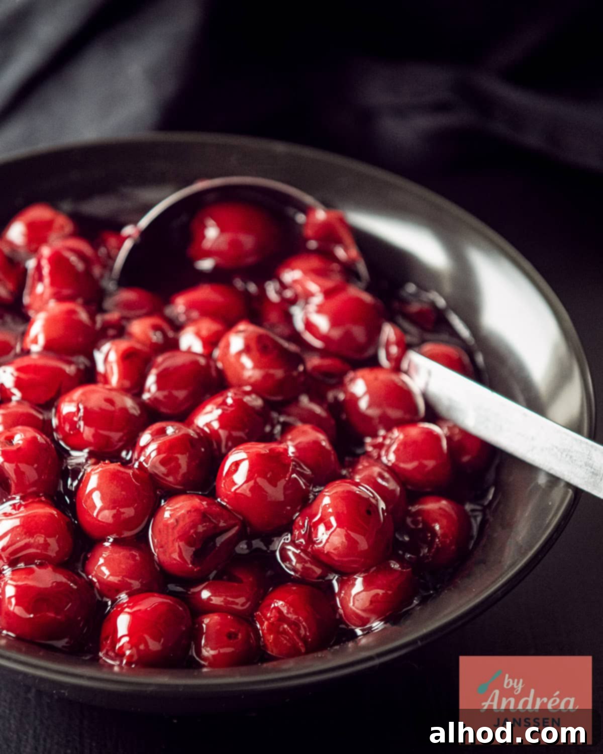 A black bowl with cherry filling for pie, garnished with a few fresh cherries.