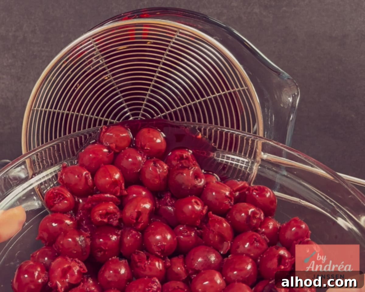 A jar of cherries is placed in a sieve to drain, with a bowl underneath to collect the syrup.