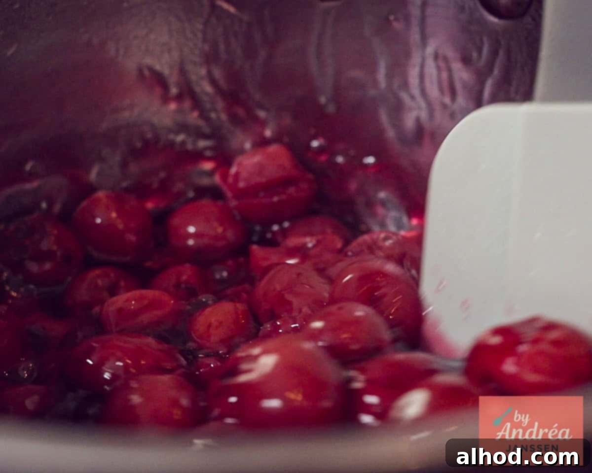 Drained cherries are added to the thickened syrup in a pan and gently stirred to combine.