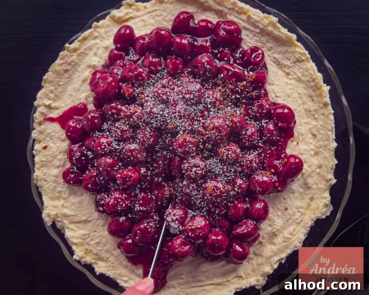A hand is shown carefully slicing a piece of the set Monchou cake, revealing its beautiful, distinct layers of crust, filling, and cherry topping.