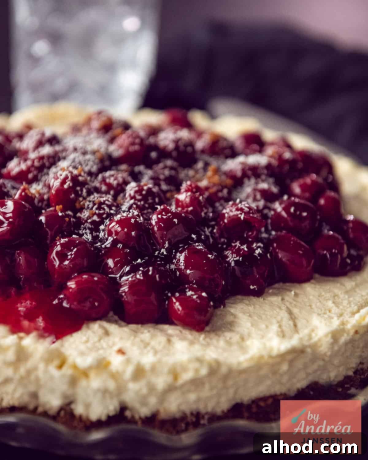 A close-up side view of a slice of Monchou cake, beautifully showcasing the three distinct layers: the dark Biscoff crust, the light cream cheese filling, and the glossy red cherry pie topping.