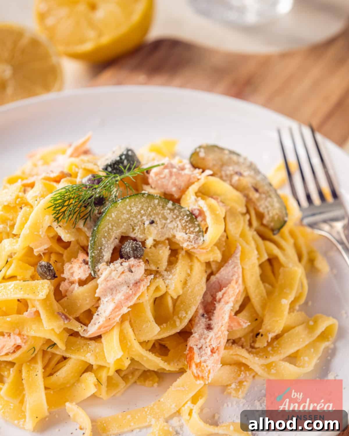 A white plate with tagliatelle, zucchini, salmon and a creamy sauce.