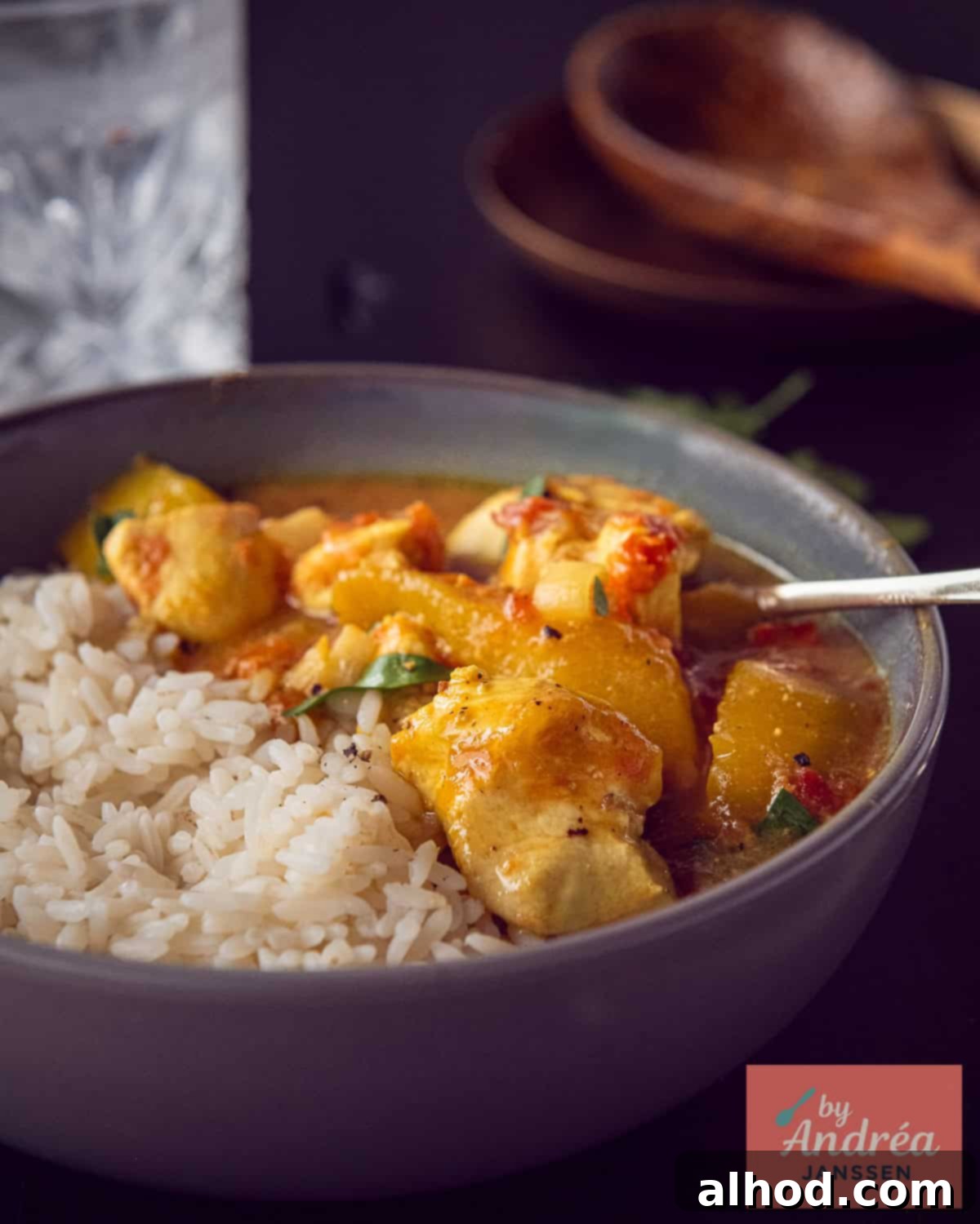 A gray bowl half filled with fluffy basmati rice and half with rich, creamy slow cooker chicken curry featuring tender chicken pieces and sweet mango in a tomato-coconut sauce, garnished with fresh cilantro.