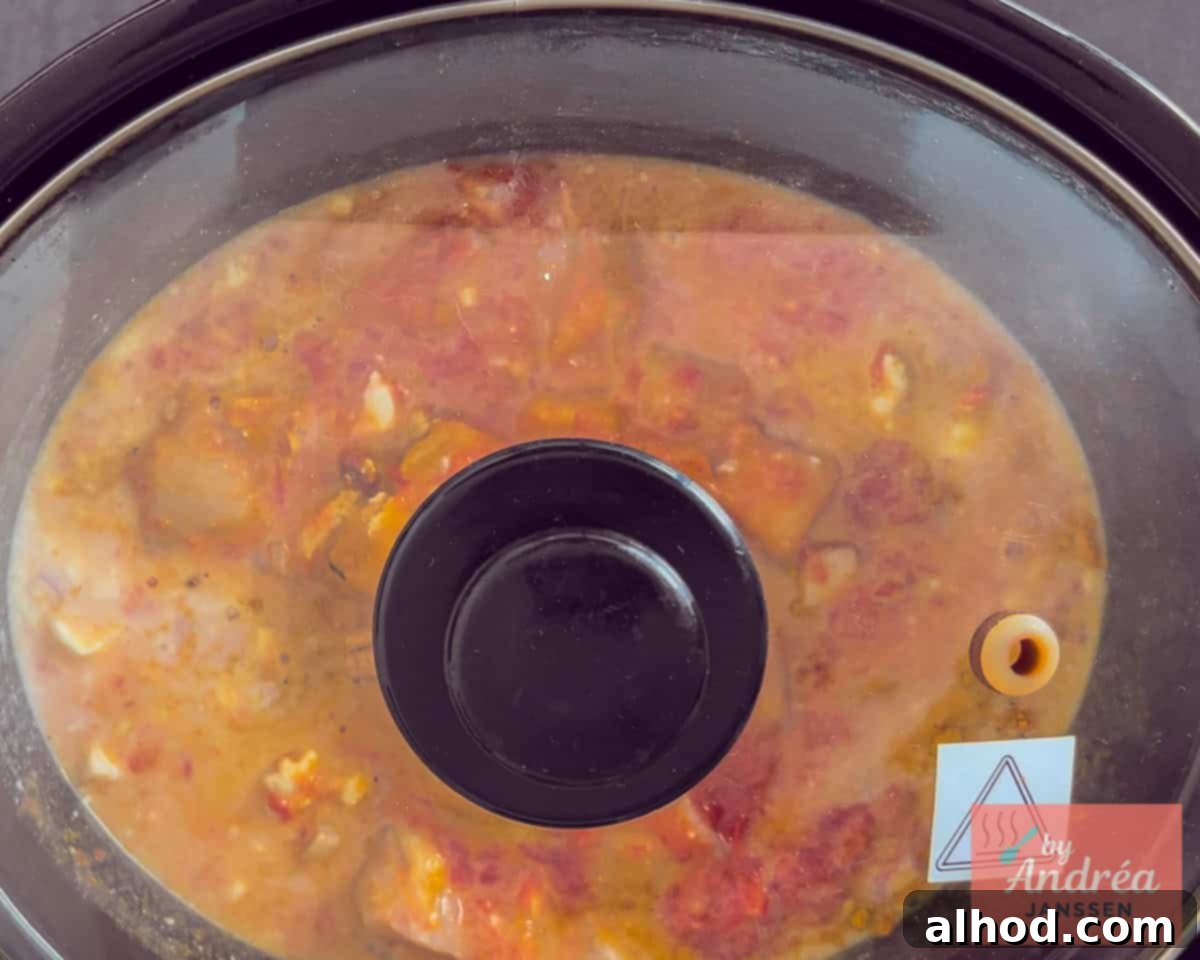 A slow cooker with the lid slightly ajar, showing a bubbling, rich chicken curry simmering gently.
