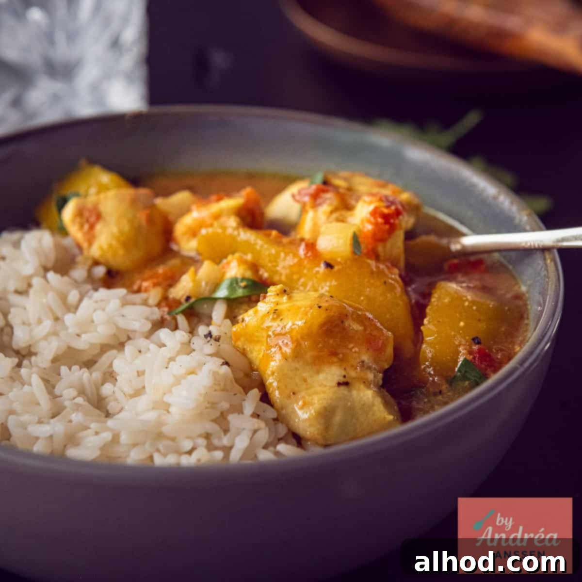 A square photo of a bowl of fluffy basmati rice, tender chicken, and sweet mango curry, garnished with fresh herbs.