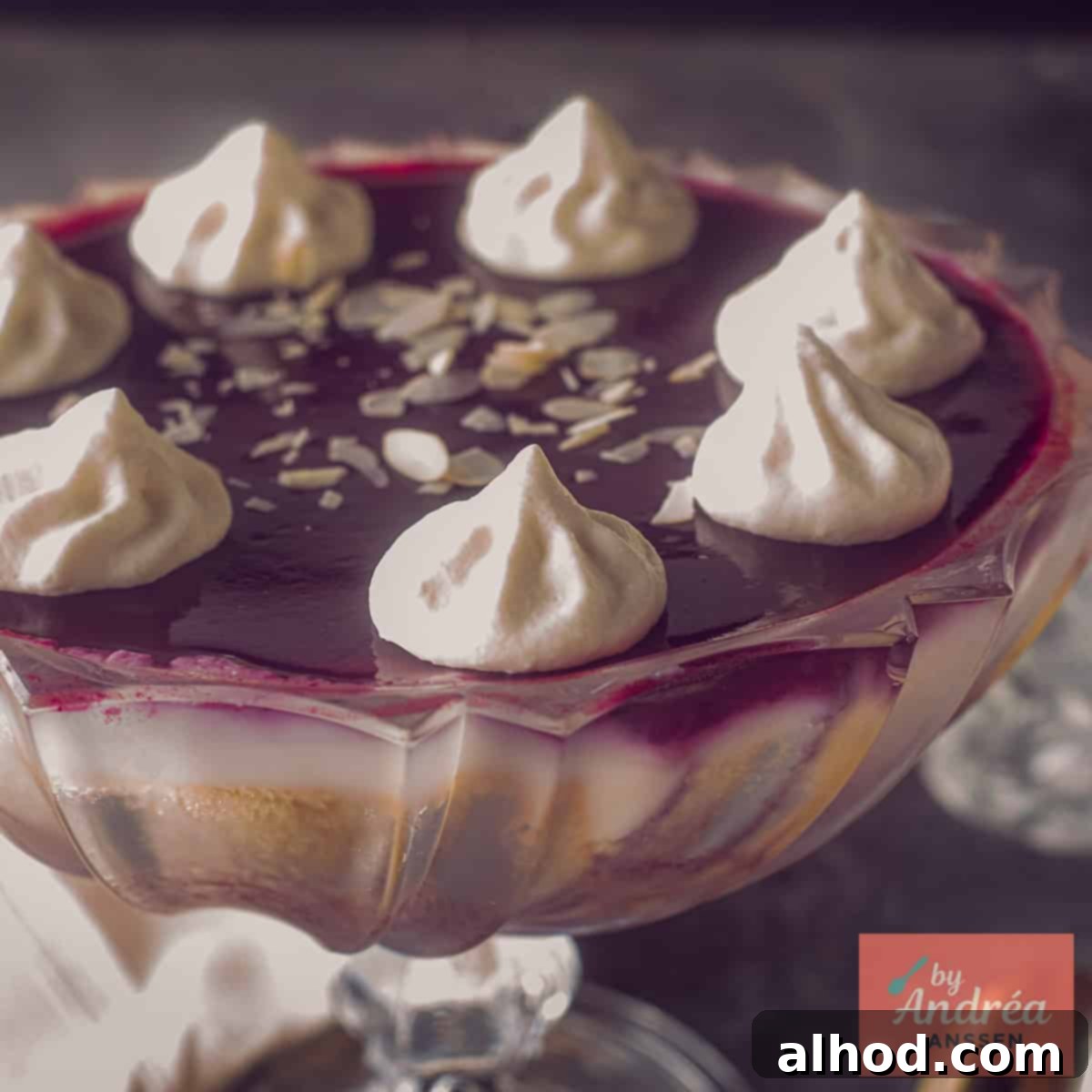 A square photo of a bowl filled with custard, cake, red fruit jelly and sherry.