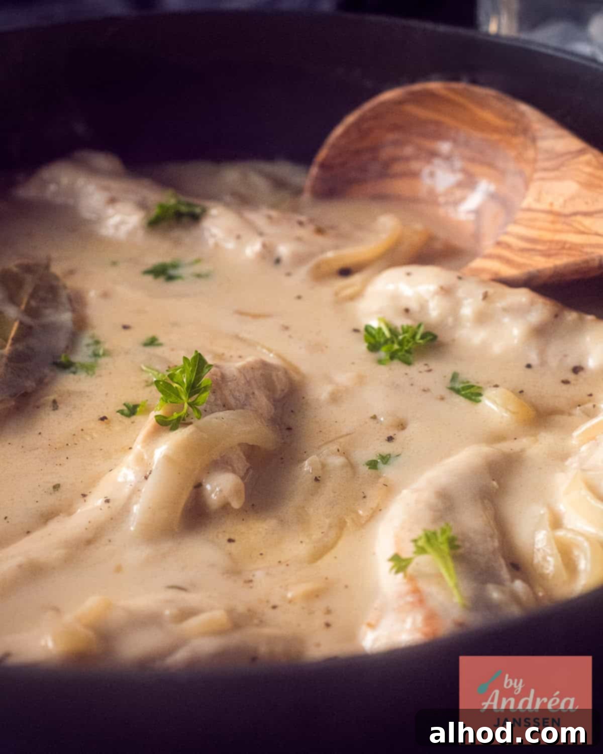A delicious pan of chicken fricassee with creamy white wine sauce, featuring visible onions and thyme sprigs, with a wooden spoon resting inside.