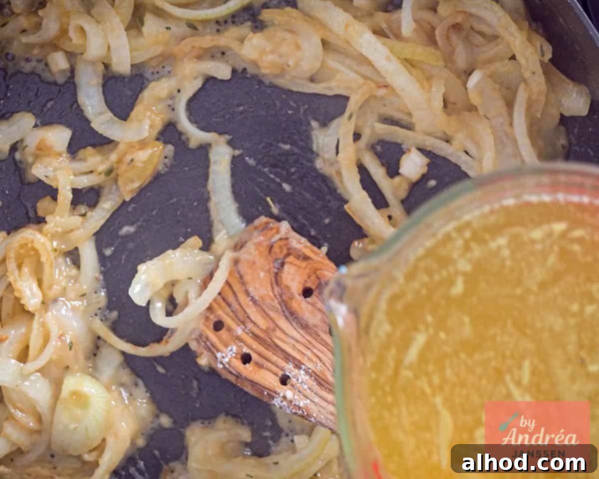 Chicken broth being poured into a pan with sauteed onions, creating the base for the creamy sauce.