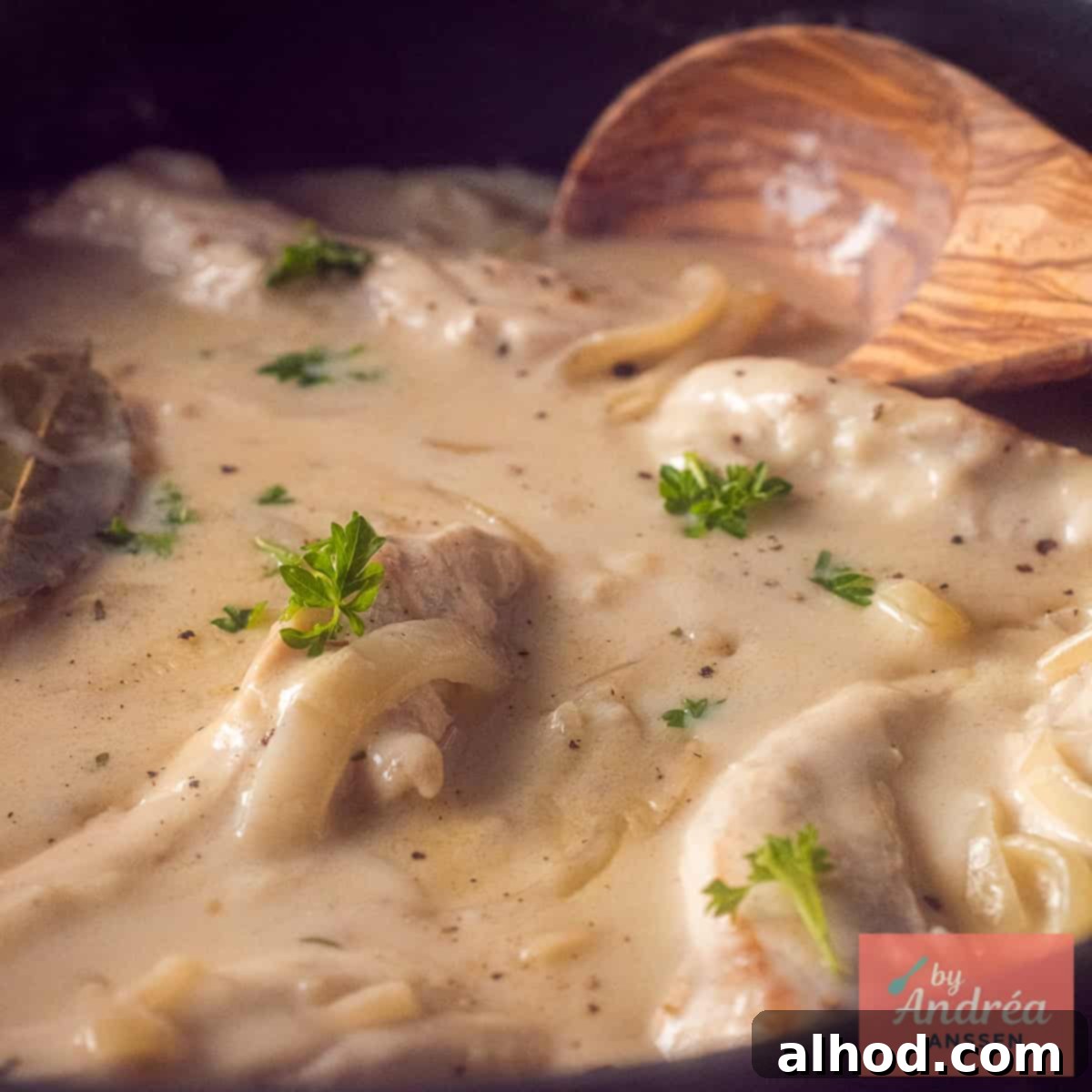 A square photo of a pan of chicken in cream sauce, with onion and white wine, showcasing the finished dish.