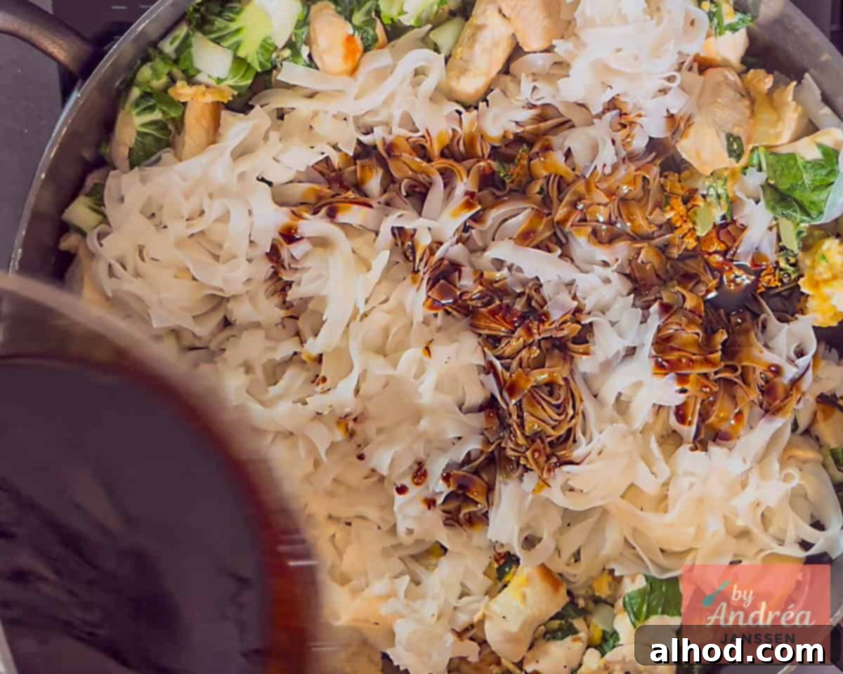 Quick Chicken Pad See Ew: 20-Minute Thai Noodle Perfection 8 Pouring the sauce over the rice noodles with chicken and bok choy for Chicken Pad See Ew