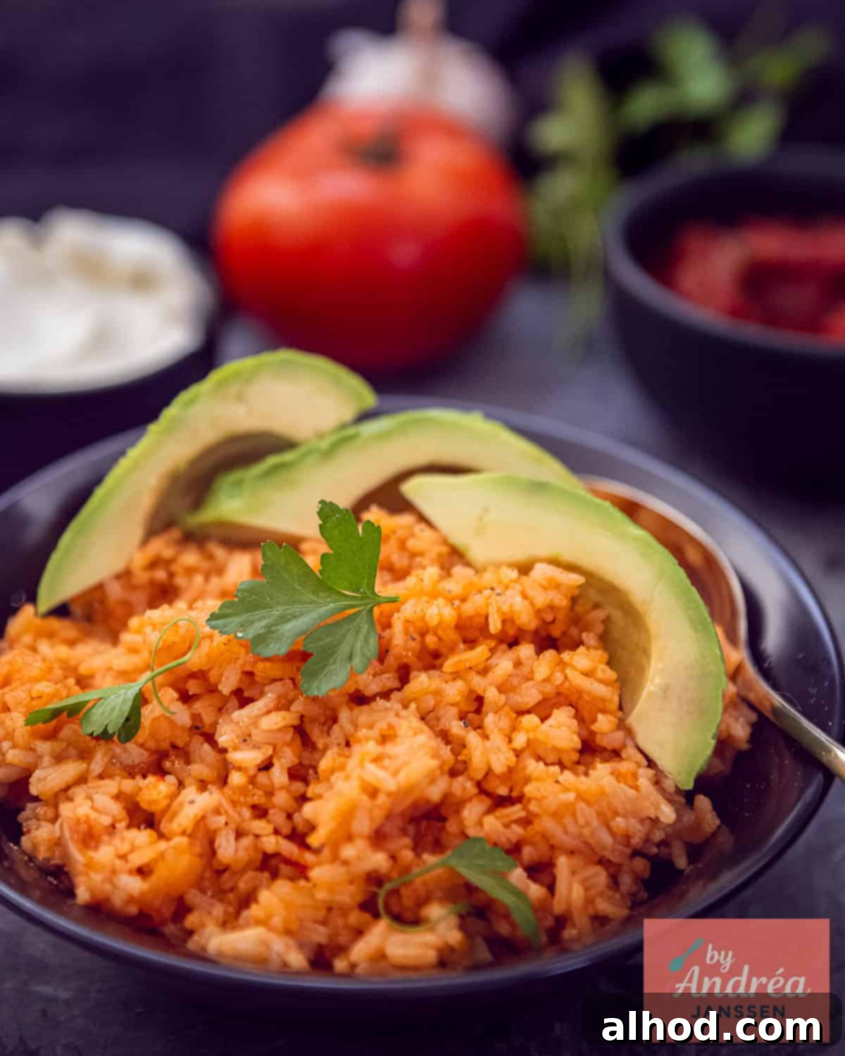 30-Minute Fiesta Rice 2 A black bowl of Mexican rice with parsley and avocado. In the background, tomato, parsley, salsa, and crème fraîche.