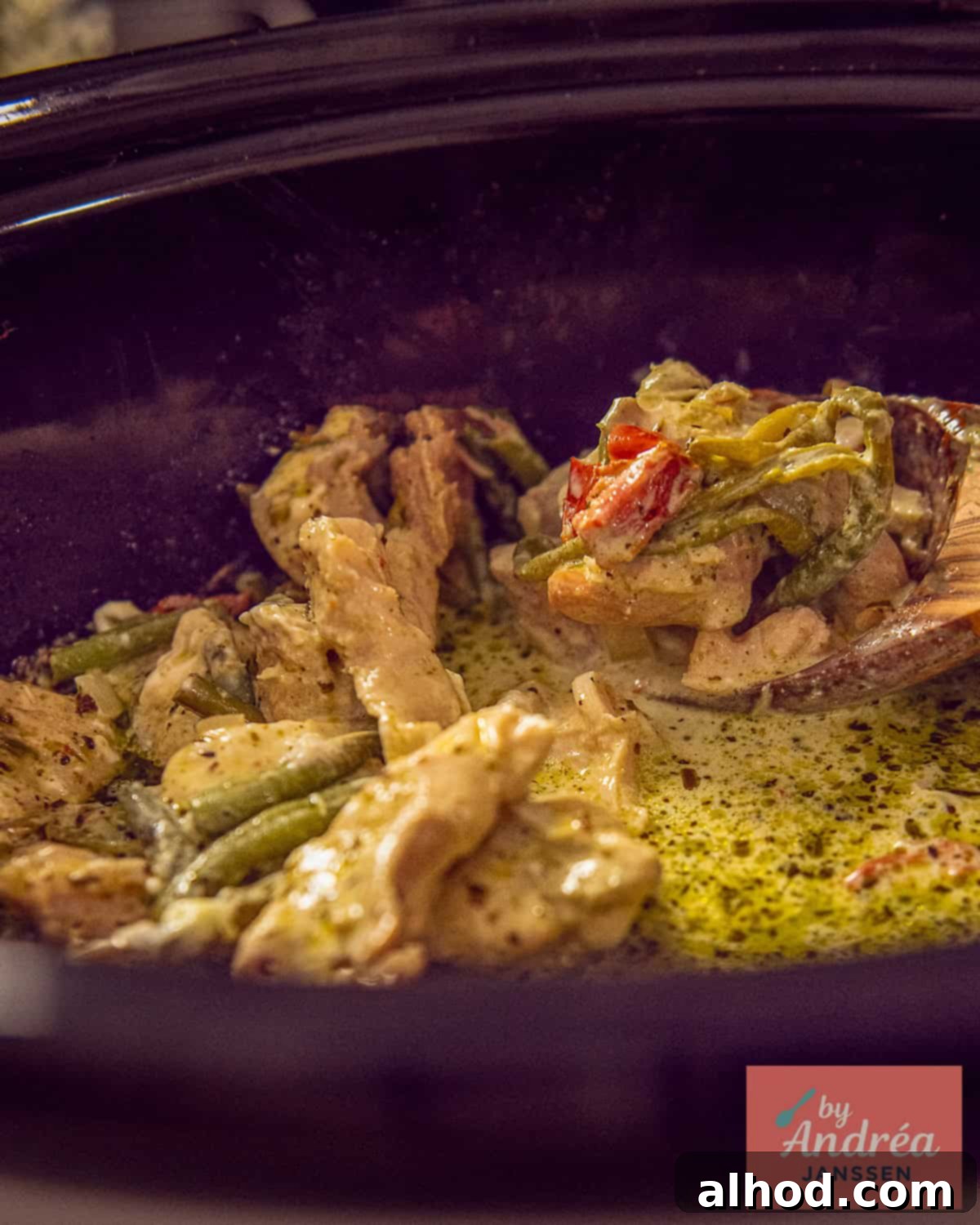Slow Cooker Creamy Tuscan Pesto Chicken 2 A bamboo spoon scoops Slow Cooker Tuscan chicken from the slow cooker, showcasing the creamy pesto sauce and tender chicken.