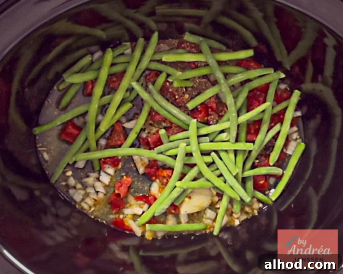 Slow Cooker Creamy Tuscan Pesto Chicken 4 Slowcooker filled with onion, tomatoes, garlic, cream and green beans, forming the base for the Tuscan chicken.